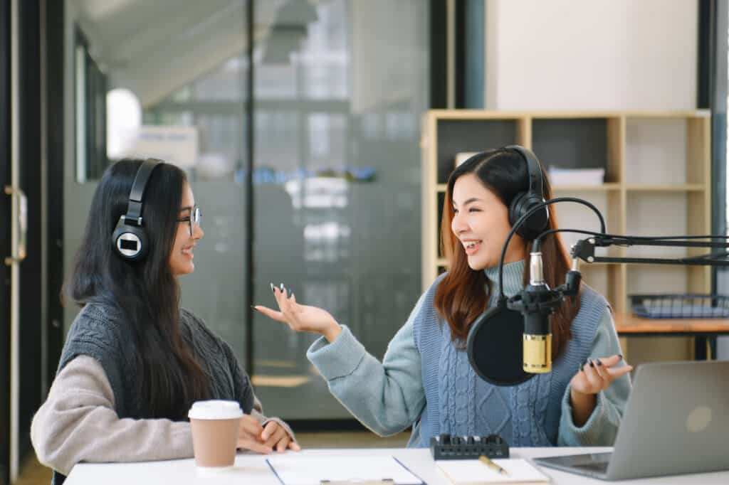 Asian woman use microphones wear headphones with laptop record podcast interview for radio. Content creator concept. in modern office