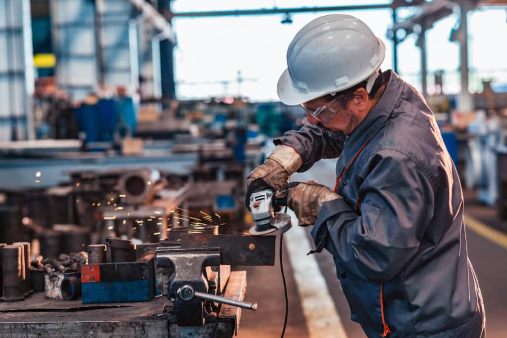 Skilled industrial worker grinding metal part.