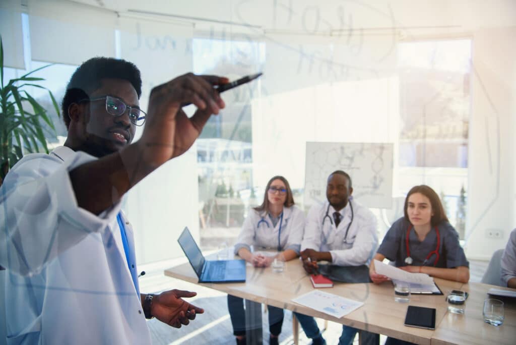 Young multiethnic interns listening lecture afro american doctor at medical conference in the clinic. During lecture the doctor writtig on board some formula for internes in the conference room at