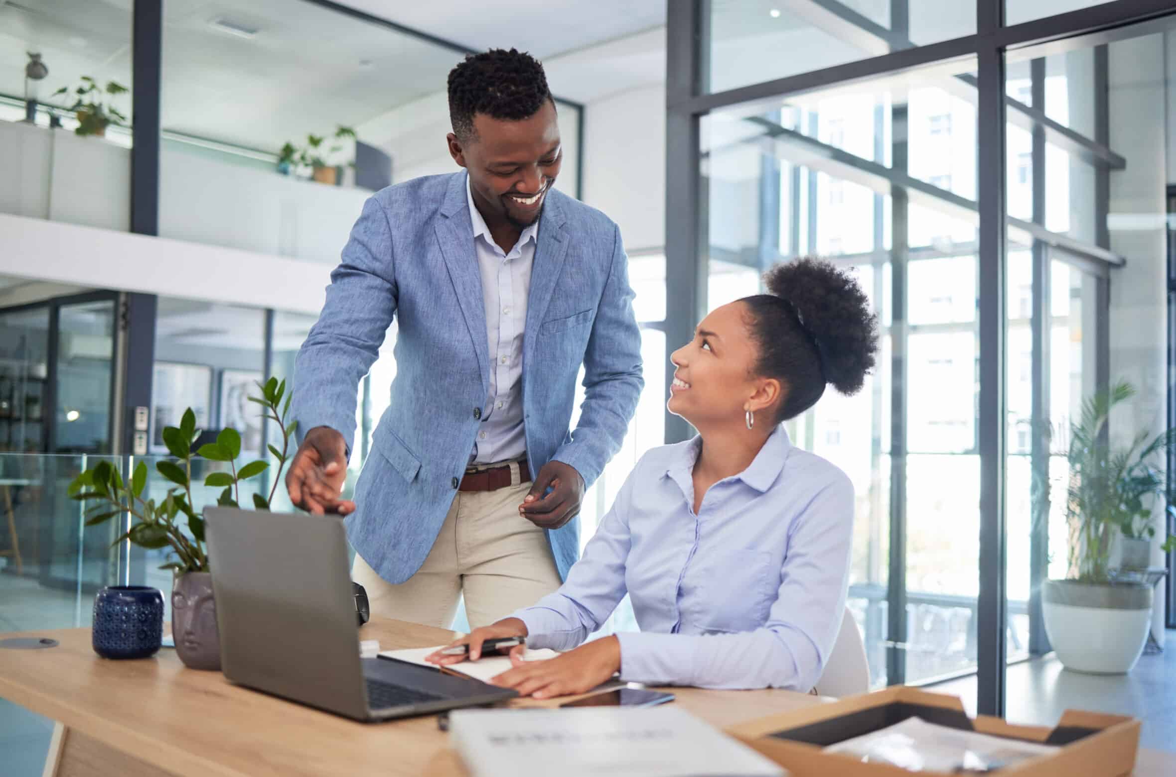 Training manager with laptop showing businesswoman how to use new software app in the office at a modern company. Smiling male mentor, trainer or boss discussing work project with employee intern