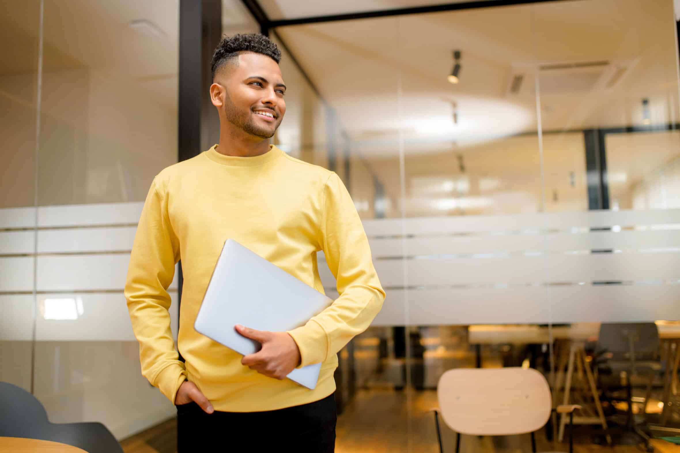 High skilled ambitious male office employee carrying laptop standing in contemporary coworking space