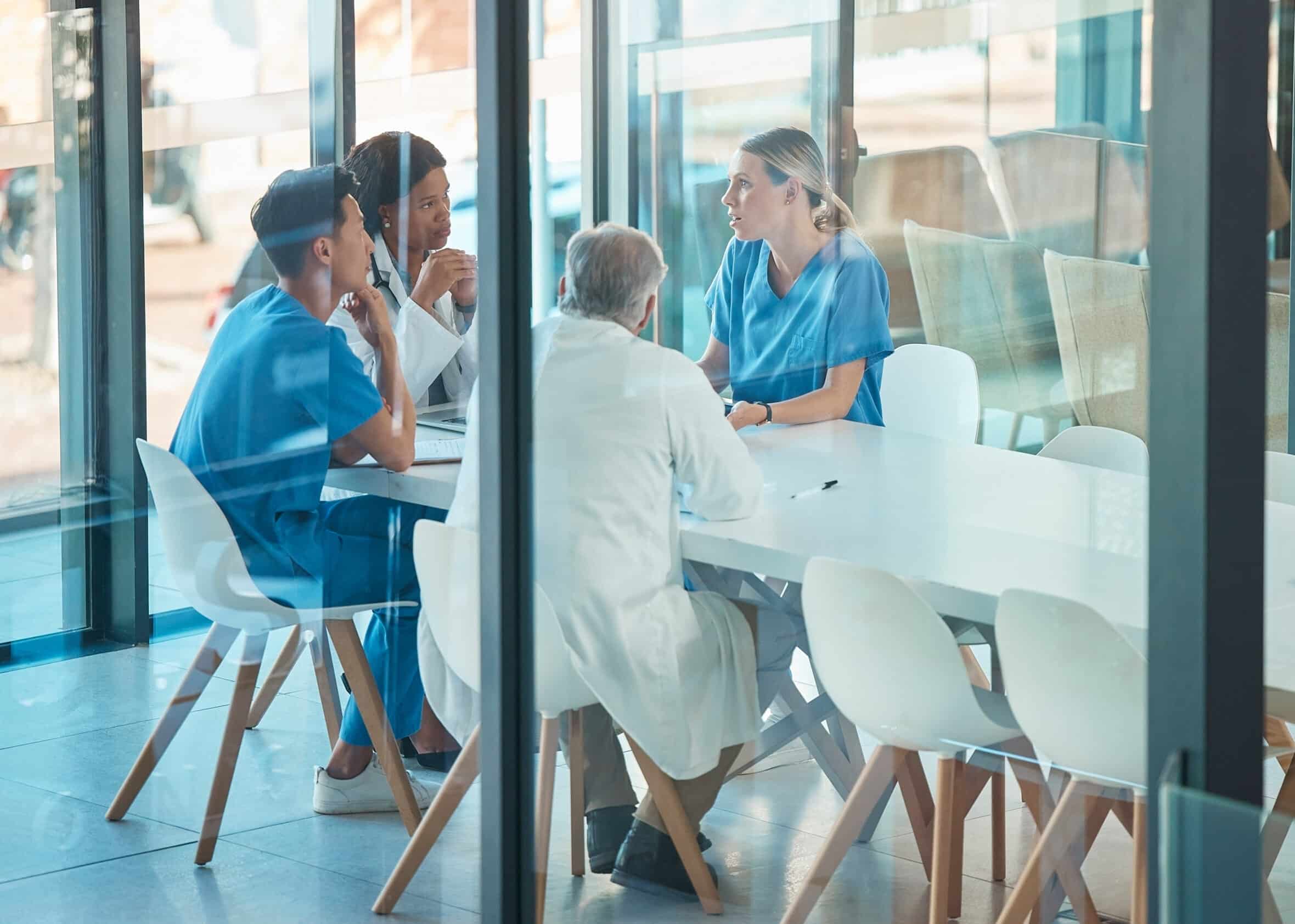 Doctors, healthcare team and meeting for a discussion, planning or training at table. Diversity men and women medical group talking about communication strategy, virus or surgery in a hospital