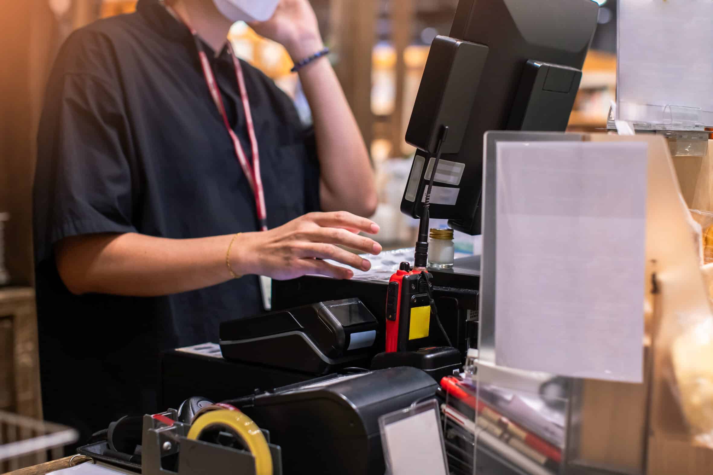 Selective focus to edge of POS machine with blurry cashier staff receive orders from customers at counter service in restaurant or cafe or department store.