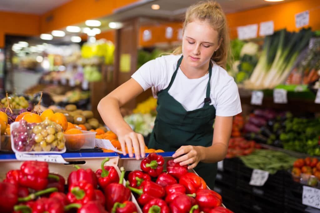 Young female seller holding pepper in grocery