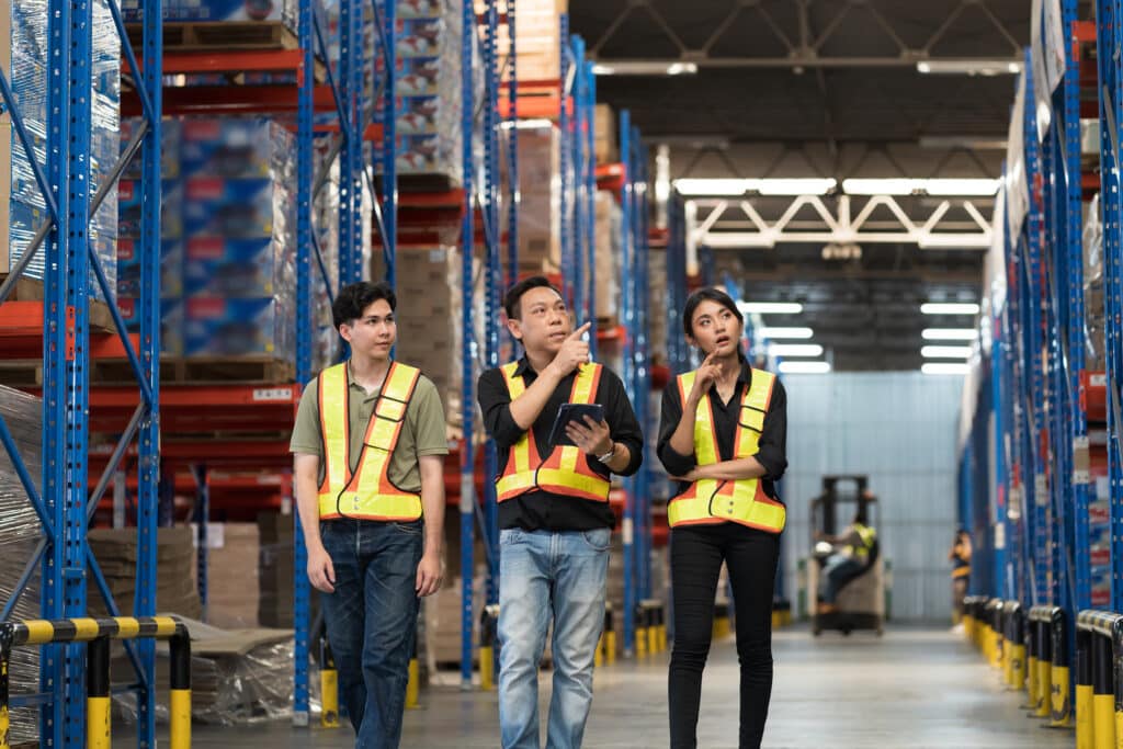 Male and female warehouse workers inspecting of product on shelf in storage warehouse. Group of warehouse workers discuss and training work in distribution branch