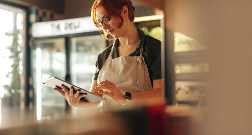 Cheerful shop owner using a digital tablet while standing in her grocery store. Successful female entrepreneur running her small business using wireless technology.