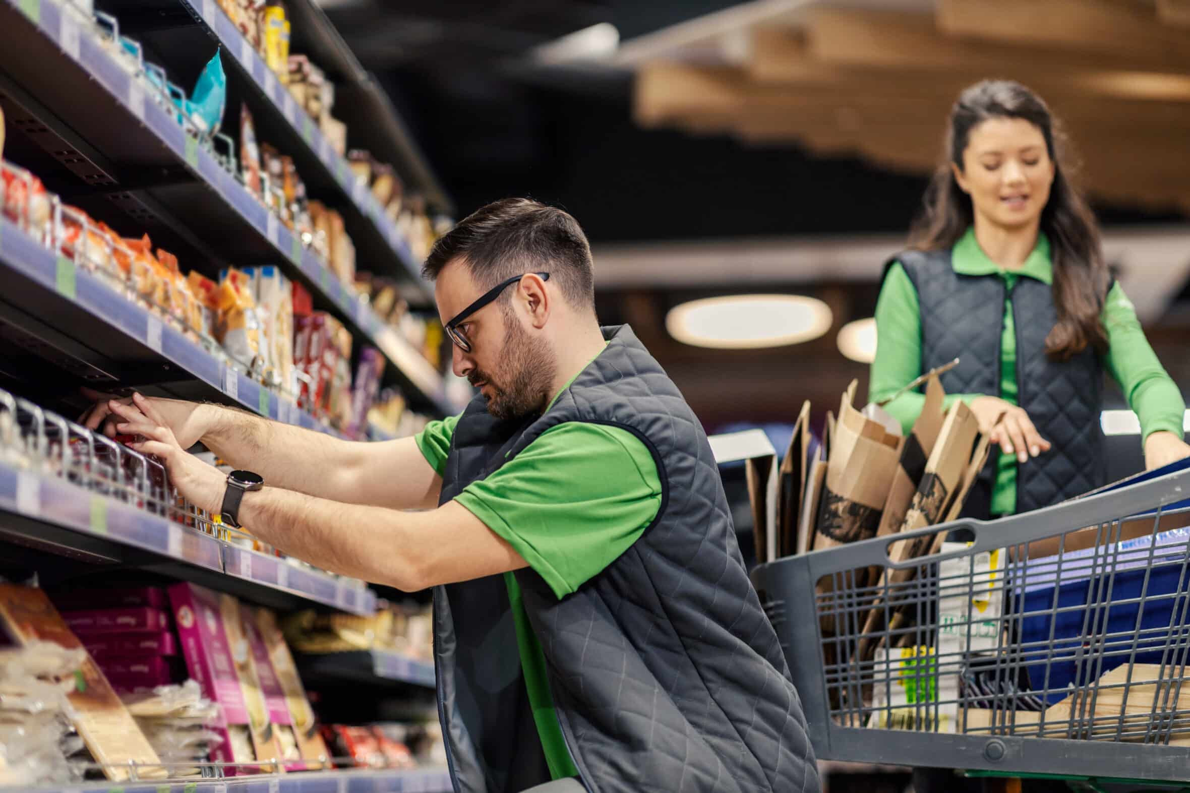 A supermarket worker is displaying groceries on shelves at marketplace.
