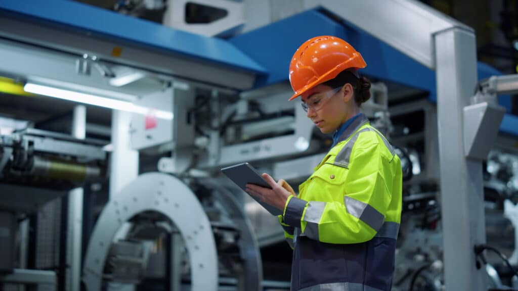 Woman supervisor looking tablet computer in huge manufacturing company. Focused industrial worker analyzing project modern plant. Safety uniform engineer check business on digital tad at factory.